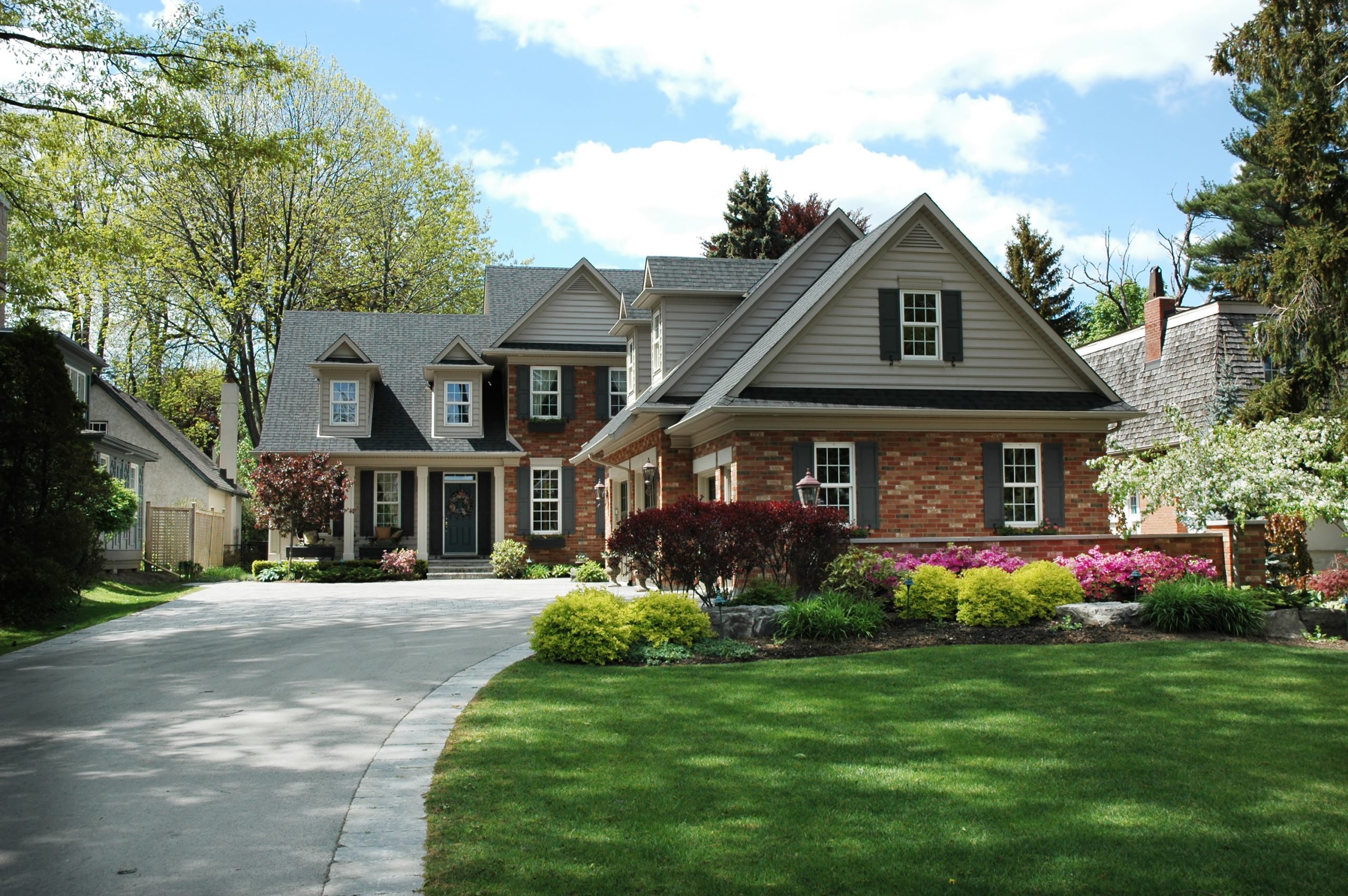 Red brick house with black shutters and pretty manicured lawn / garden